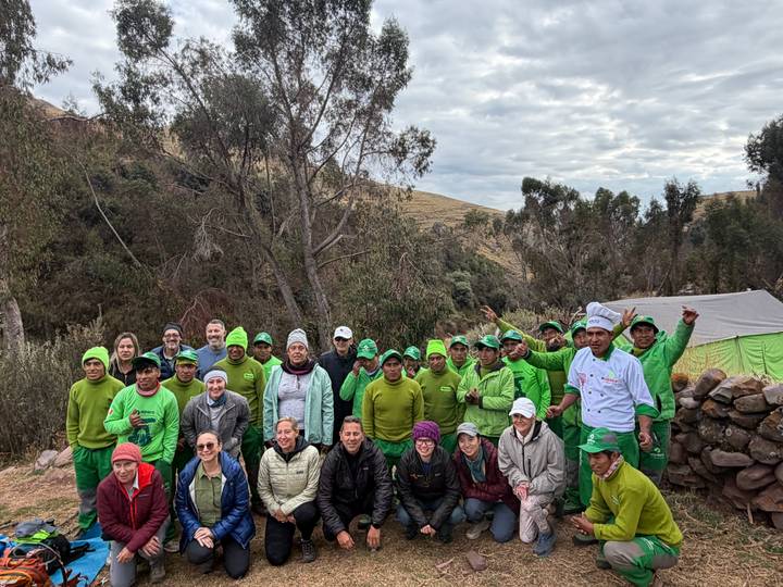 Large trekking team of porters, cooks and hikers in green uniforms pose cheerfully at a mountain campsite.