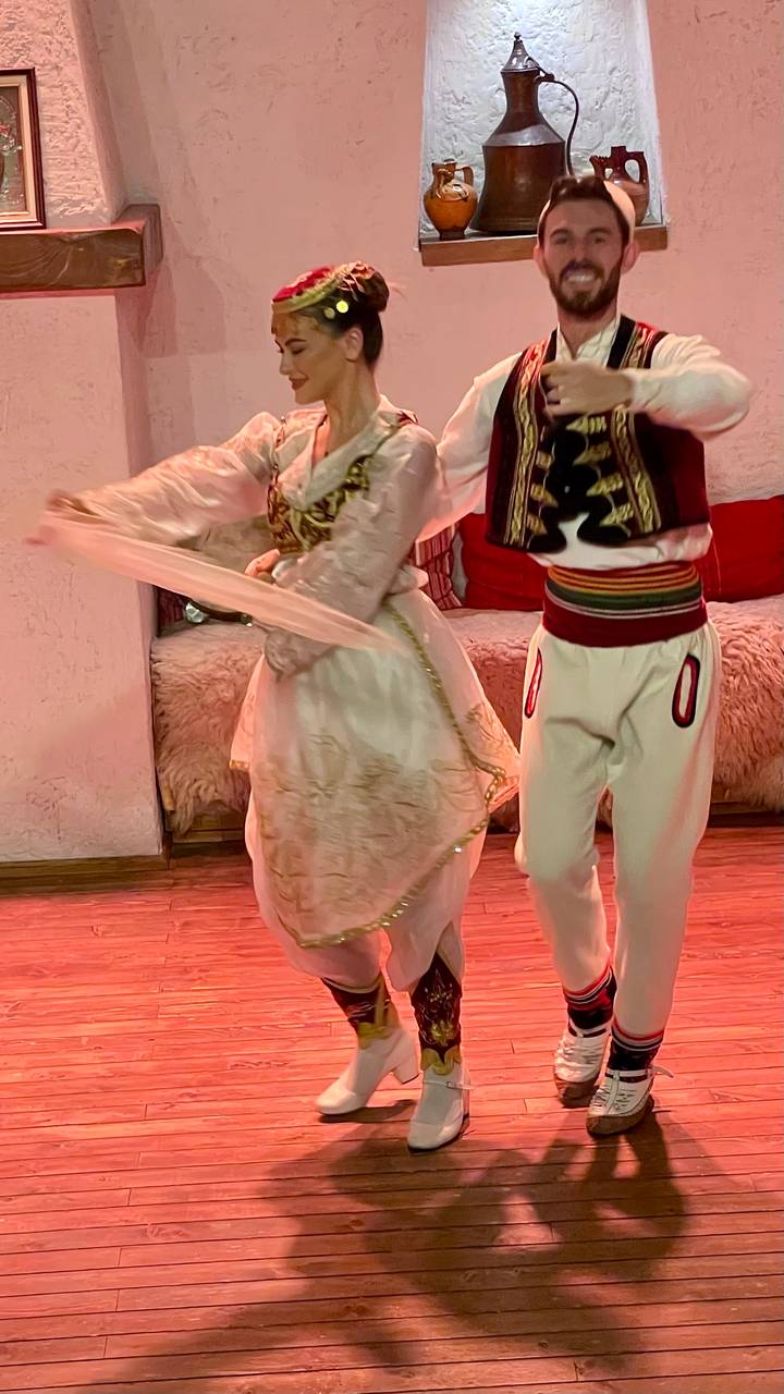 Close-up of traditional Albanian dancers in embroidered costumes moving across a wooden floor.