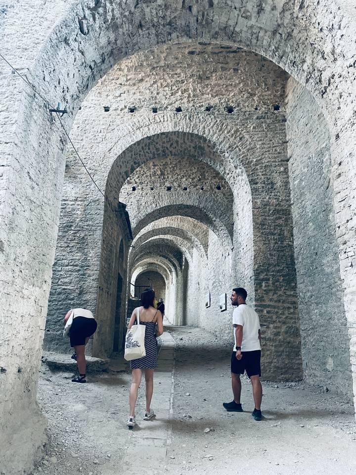Visitors walk through a long vaulted stone corridor of an ancient fortress or castle.