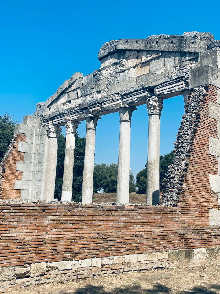 Ruins of an ancient Roman temple with intact marble columns against a bright blue sky.