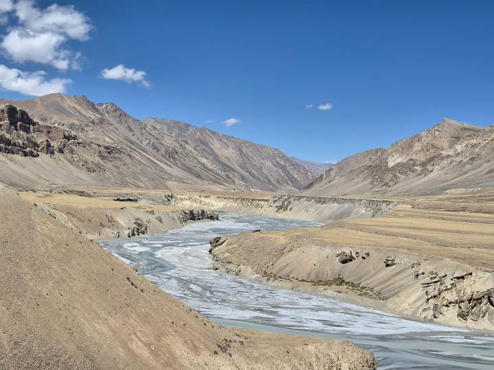 Wide barren valley with braided grey river cutting through rugged desert mountains