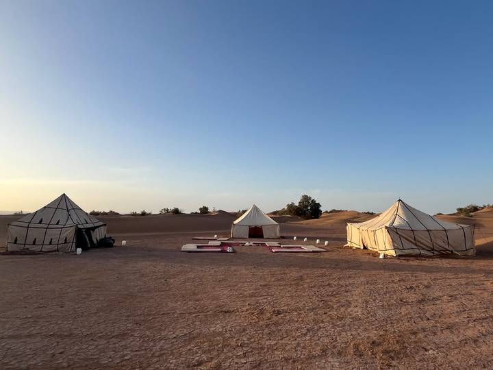Remote desert camp with three canvas tents set among golden dunes under a clear blue sky.