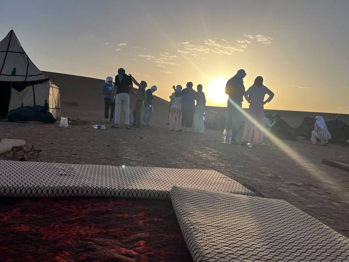 Silhouetted group chatting near camels at sunset in the desert camp.