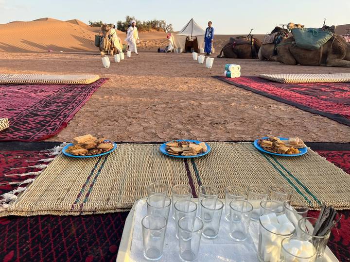 Low tables with biscuits and tea glasses arranged on mats at a desert campsite.