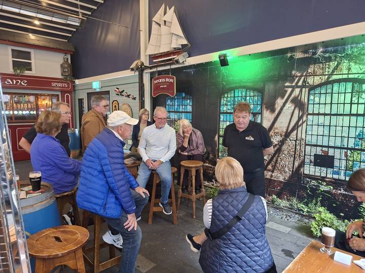 Travelers listen to local guide inside atmospheric Irish pub or distillery bar.