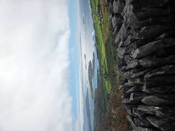 Atlantic coastline and green patchwork fields viewed over a stone wall on a cloudy day
