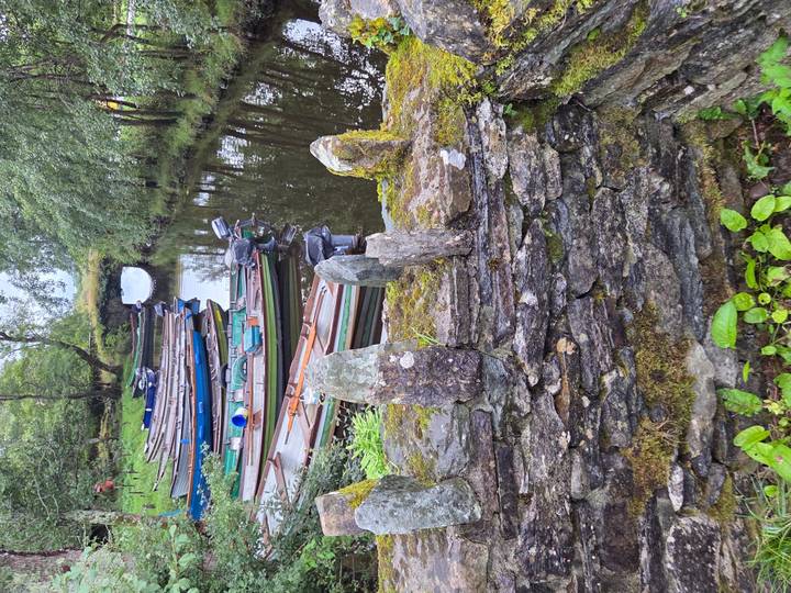 Row of wooden rowing boats moored on a calm narrow canal beside mossy stone wall