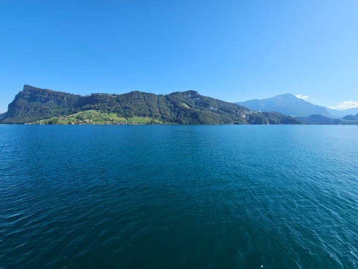 Deep-blue lake framed by forested slopes and distant alpine peaks under a cloudless sky