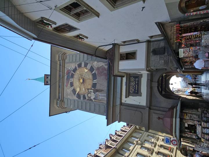 Tall medieval clock tower gate in Bern with painted astronomical dial and shoppers passing beneath