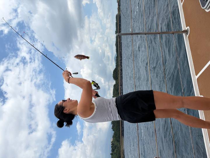 Young woman reeling in a fish while standing on a yacht deck on open sea.