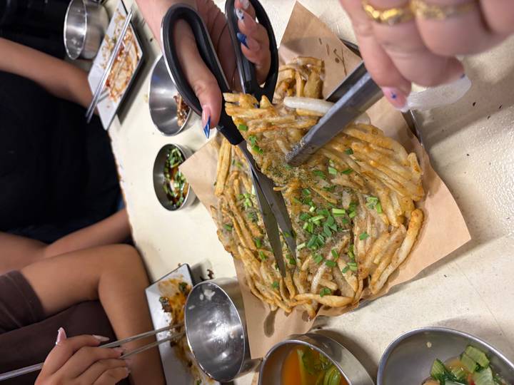 Shared Korean seafood pancake being cut with scissors at a casual night-market table.