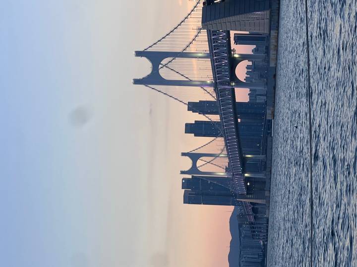 Gwangan Bridge and modern Busan skyline glowing at pastel sunset over calm bay.