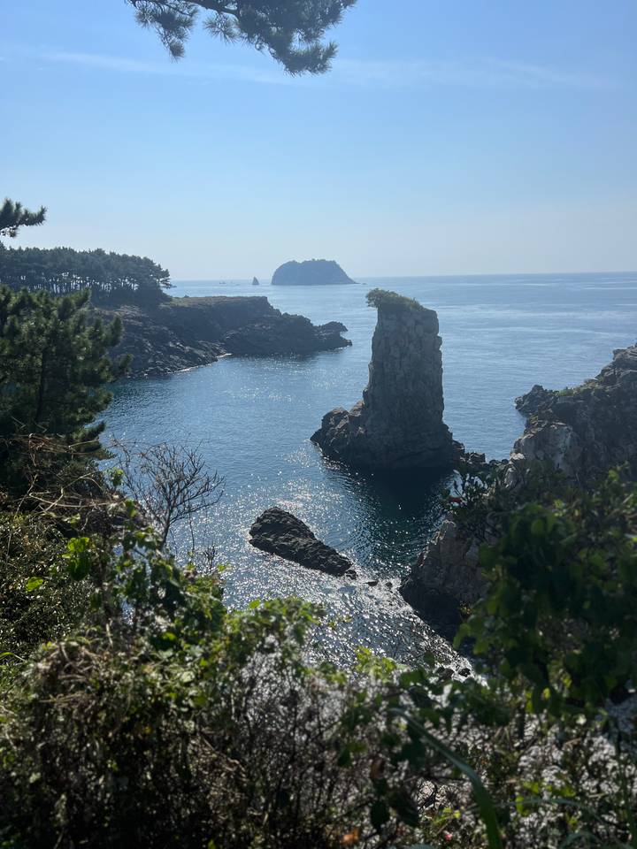 Dramatic sea stack and sparkling blue water off rugged Jeju Island coastline.