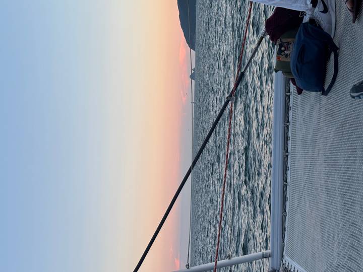 Peaceful sunset from a catamaran deck over calm sea and pastel horizon.