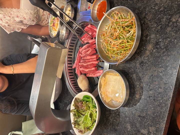Korean BBQ grill with marbled beef and fresh side dishes ready to cook at the table.