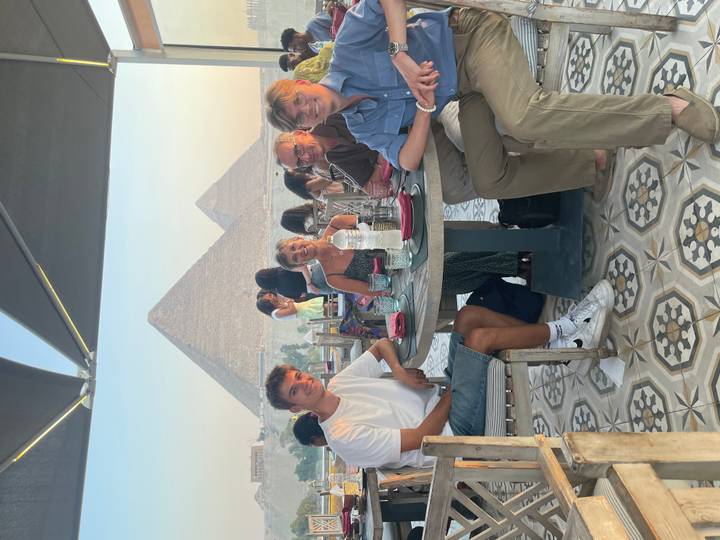 Family dining at a rooftop restaurant with two iconic pyramids of Giza towering in the hazy background at golden hour.