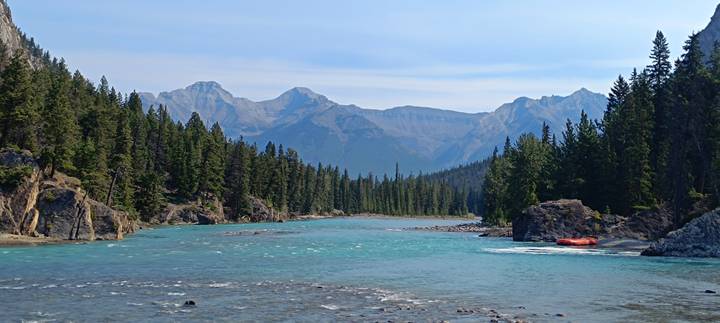Turquoise river winding through pine forest with inflatable raft on shore