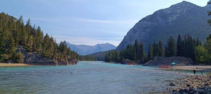Wide alpine river flowing through conifer forest with mountains framing the valley