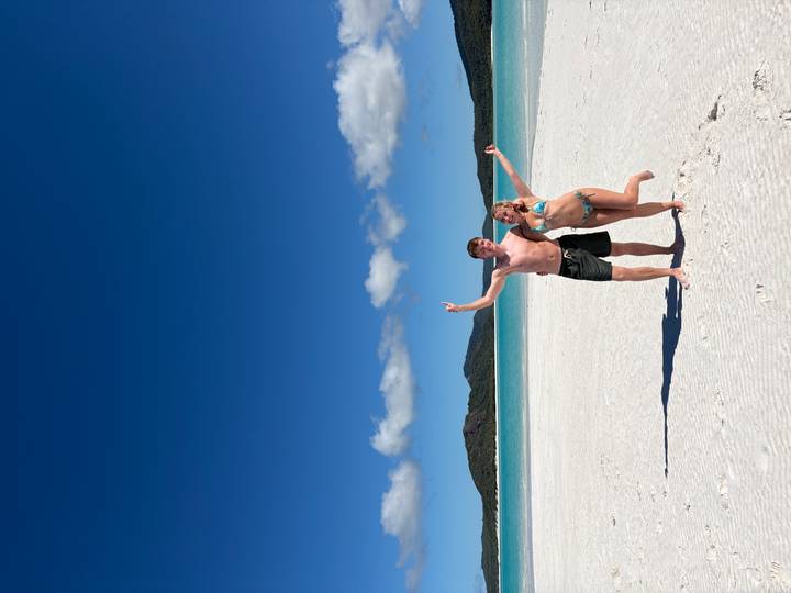 Couple celebrate on the white silica sands of Whitehaven Beach with crystal-clear turquoise water behind.