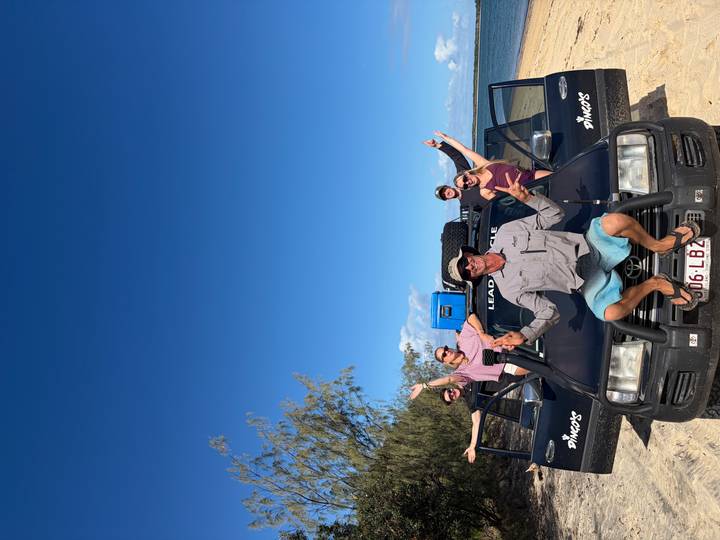 Tour guide and travellers enthusiastically pose with arms outstretched on a 4x4 tour vehicle.