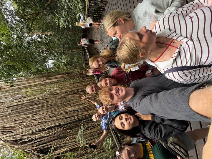 Travellers pose for a selfie along a rainforest boardwalk beside massive hanging roots.