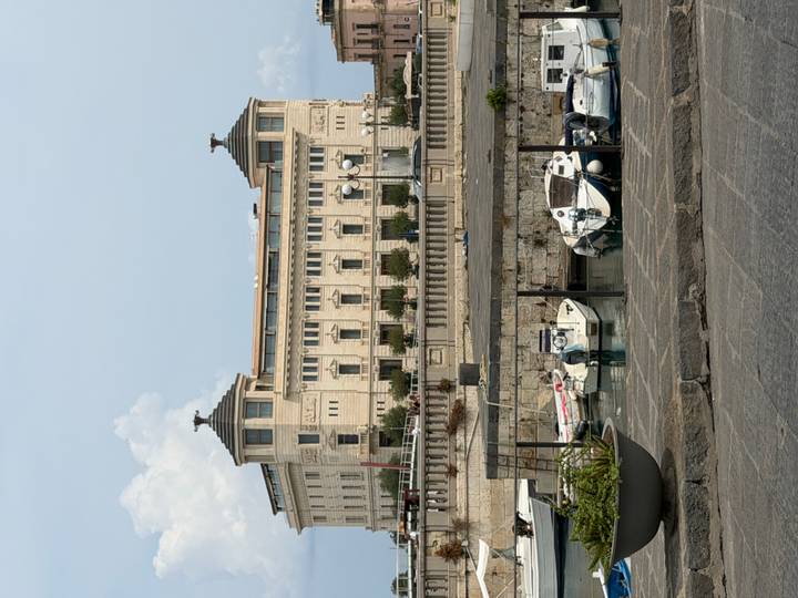Elegant neoclassical waterfront building faces a small marina filled with white motorboats.