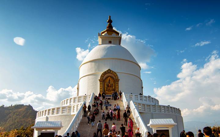 Visitors climb wide staircases to a white Peace Pagoda crowned by a golden spire under blue skies.