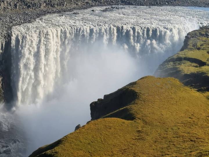 Powerful curtain of water plunging over Dettifoss waterfall with mist rising beside mossy cliffs