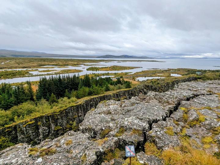 Rift valley with rocky ledge, conifer forests and winding waterways under a cloudy Icelandic sky
