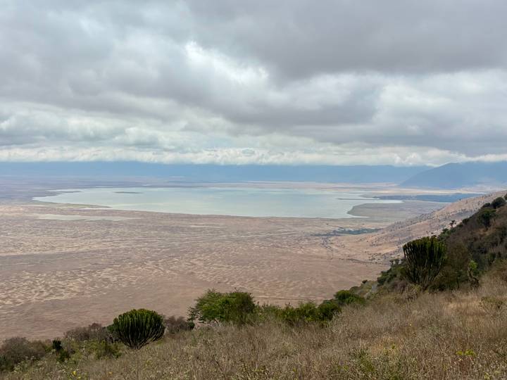 Expansive view from crater rim over a broad lake and patterned plains beneath a cloudy sky.