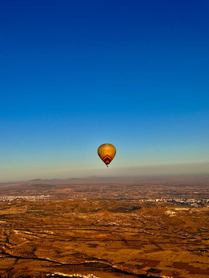 Yellow balloon floats solo high above Cappadocian plateau under a clear blue sky.