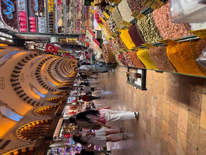 Busy indoor spice bazaar lined with colorful mounds of herbs and sweets under ornate arched ceiling.