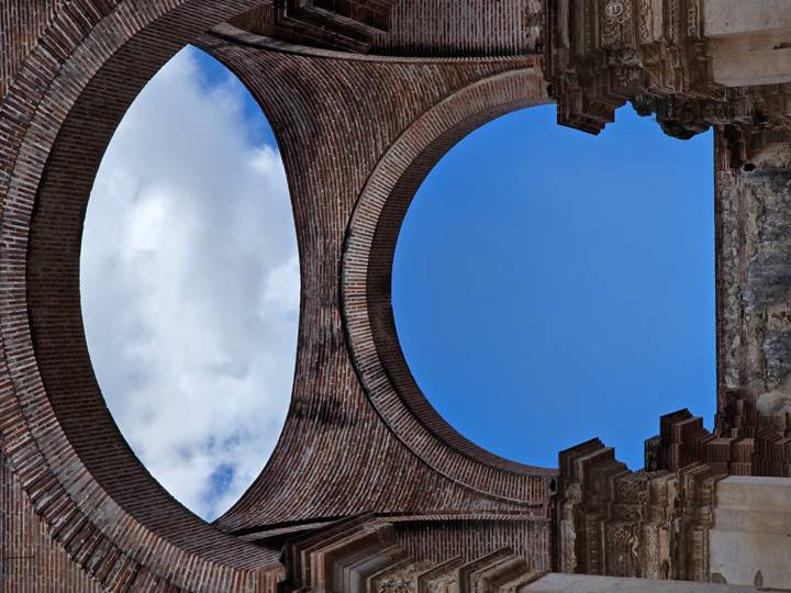 Looking up through a massive brick archway of an Antigua ruin to a patch of blue sky and clouds.