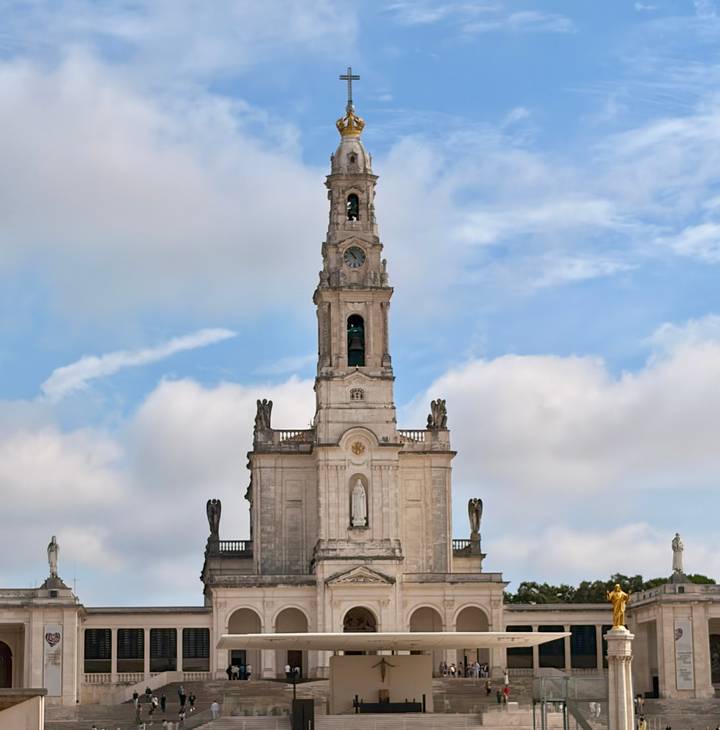 Tall church tower with clock and statue details rises against a blue sky with scattered clouds.