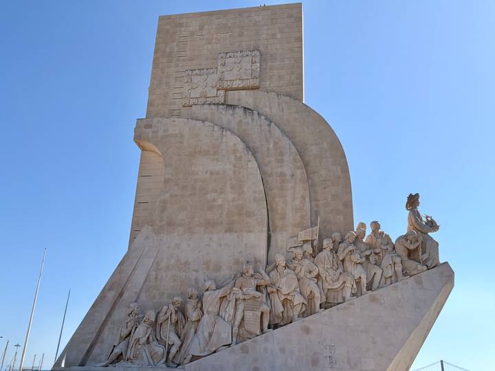 Monument of stone sailors on a ship-shaped pedestal reaching into a clear blue sky.