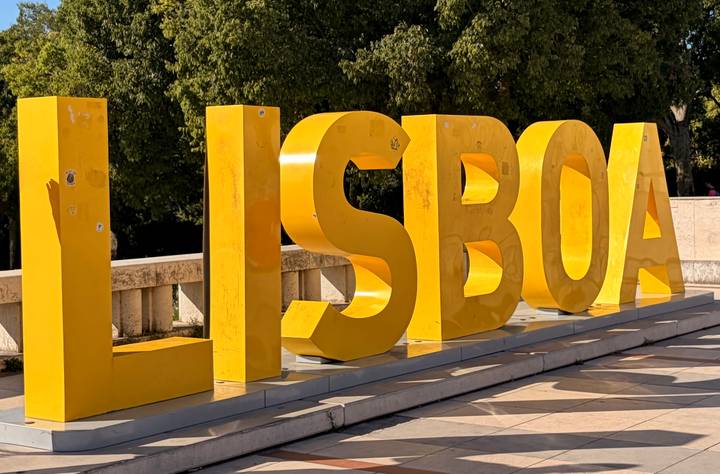 Bright yellow 3D letters spelling LISBOA in an outdoor plaza.