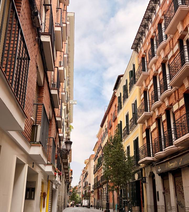 Narrow Madrid street framed by tall brick and pastel buildings with balconies.