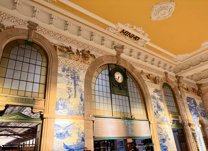 Interior hall with ornate azulejo tile murals, high arched windows and classic station clock.