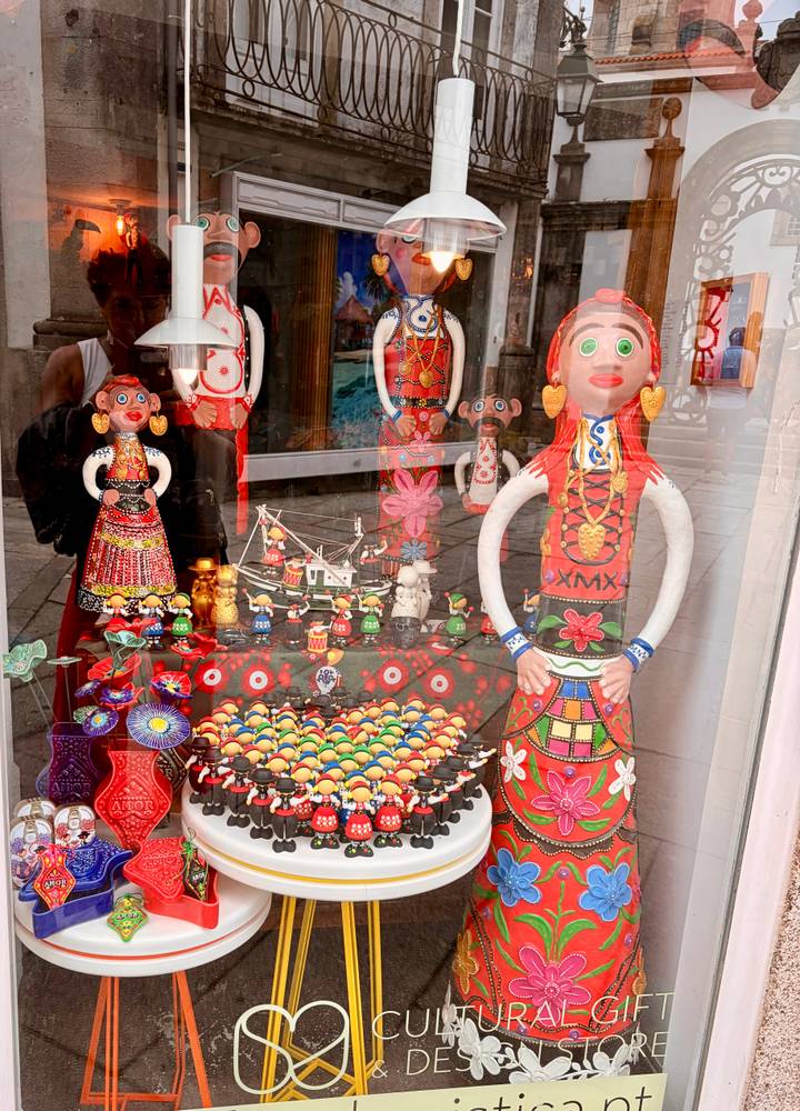 Shop window filled with colorful folk art dolls, ceramics and reflections of the street.