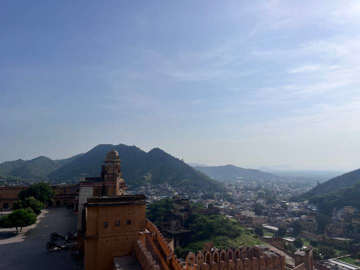 Expansive panorama of Jaipur city framed by fort walls and green hills under a clear sky.