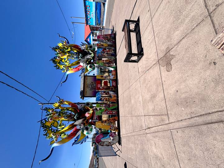 Colorful Candelaria festival sign decorated with large artistic masks on a plaza under bright blue sky.