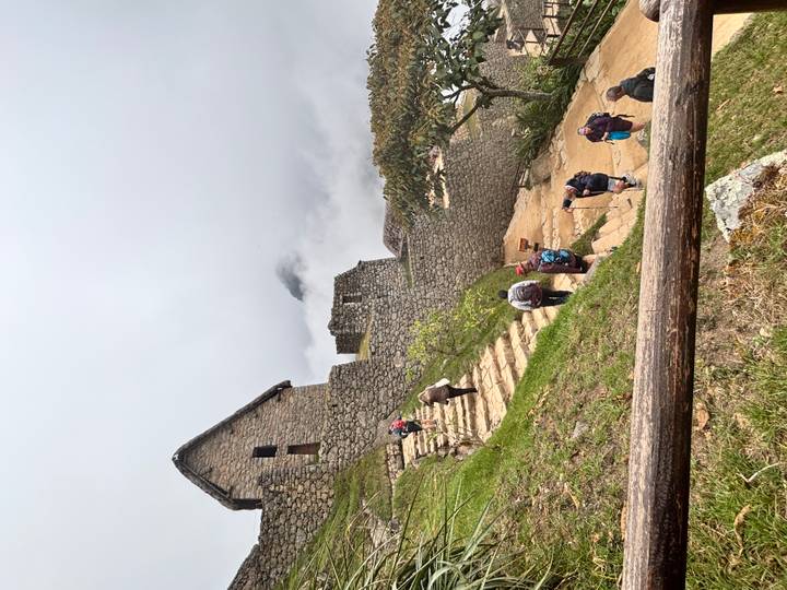 Hikers ascending stone steps among ancient ruins shrouded in mist at Machu Picchu.