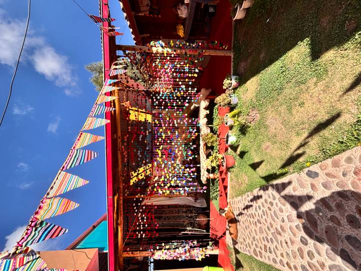 Colorful open-air craft stall decorated with hanging ornaments and striped bunting under a bright blue sky.