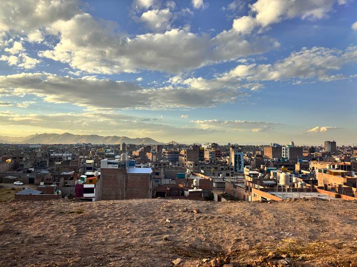 Panoramic view over a sprawling city with distant mountains beneath a partly cloudy, golden-hour sky.