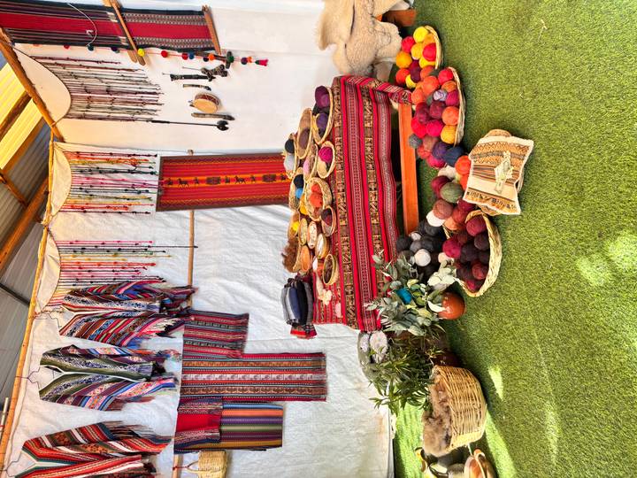 Indoor display of vibrant woven textiles and baskets of dyed wool balls on artificial grass.