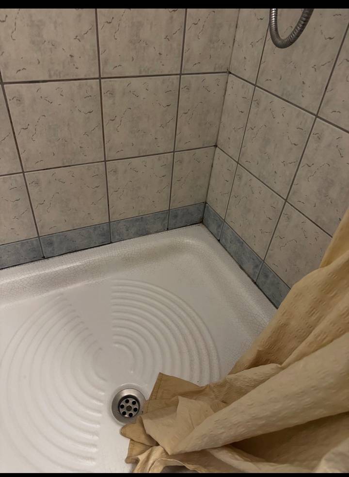 Close-up of dated tiled shower base with stained grout in a bathroom corner.