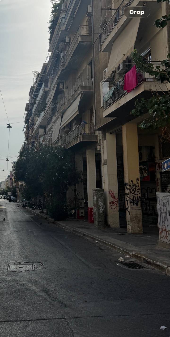 Graffitied urban street lined with drab, ageing apartment blocks and overgrown trees.