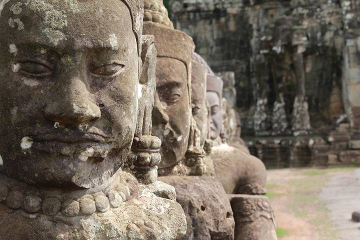 Row of ancient sandstone guardian statues with serene faces at Angkor temple complex.