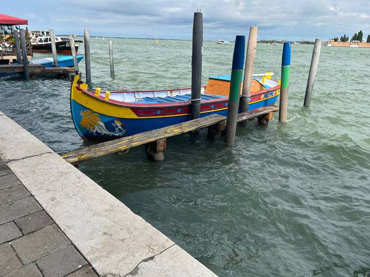 Colorful traditional wooden boat moored between poles on choppy green lagoon waters.