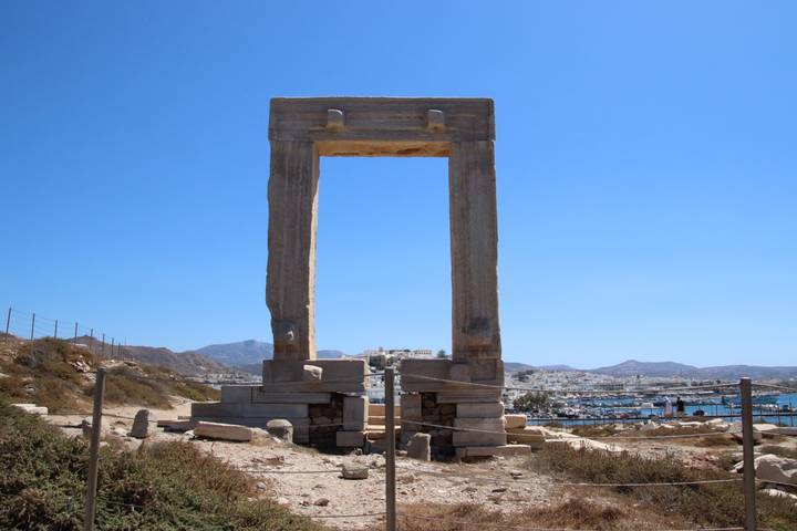 Ancient marble Portara gate of Naxos standing alone on a hilltop with harbor and town in background.